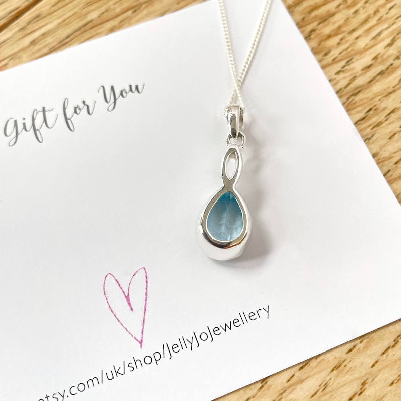 May include: A silver necklace with a teardrop-shaped pendant featuring a light blue gemstone. The pendant has a delicate, twisted design. The necklace is displayed on a white card with the text "gift for you" and a pink heart.