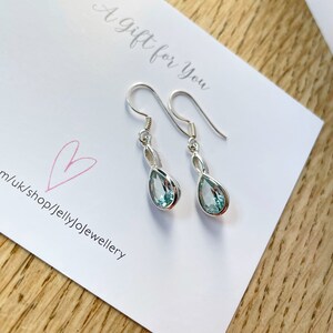 May include: A pair of silver teardrop earrings with light blue gemstones. The earrings are on a white card with the text "A Gift for You" and a pink heart.