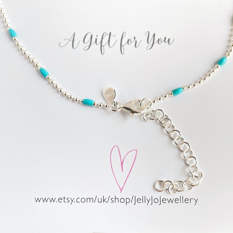 May include: A delicate silver necklace with small turquoise beads and a lobster clasp. The necklace is displayed on a white background with the text "A Gift for You" and a pink heart.