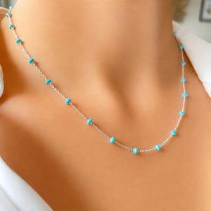 Op de afbeelding: Een delicate zilveren ketting met kleine, ronde turquoise kralen gelijkmatig verdeeld over de ketting. De ketting wordt getoond op de hals van een persoon, wat de eenvoudige elegantie benadrukt. De turquoise kralen voegen een vleugje kleur toe.