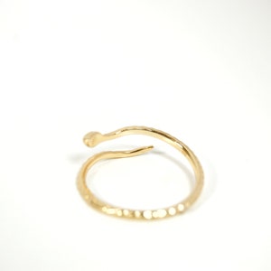 May include: A gold-toned ring with a textured, snake-like design. The ring is open and wraps around the finger.