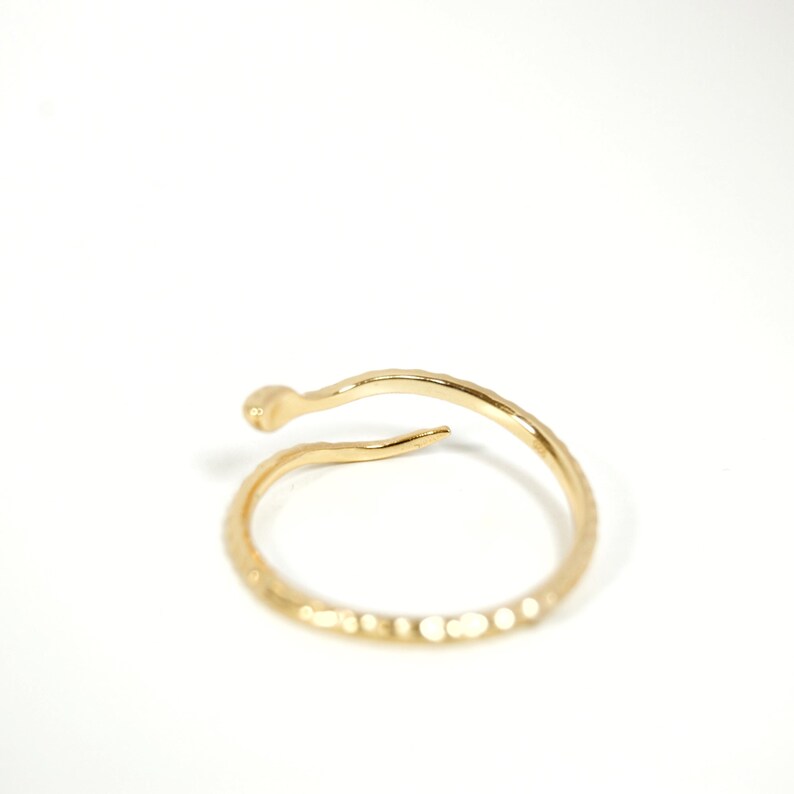 May include: A gold-toned ring with a textured, snake-like design. The ring is open and wraps around the finger.