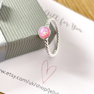 May include: A silver ring with a pink opal gemstone. The ring has a twisted band and is on a white card with the text "Gift for You" and a website address.
