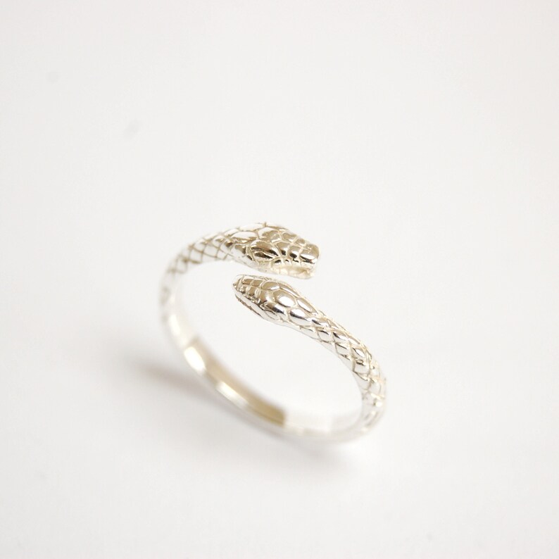 Silver ring with a snake head at each end crossing over. The ring has a snake skin pattern. The ring is adjustable as the heads are not fixed