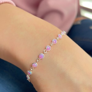 Puede incluir: Un delicado brazalete de cadena de plata con pequeñas piedras de ópalo rosa. El brazalete está en la muñeca de una persona.