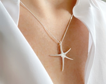 Può includere: Una collana d'argento con un ciondolo a forma di stella marina. La collana è indossata da un manichino che indossa una camicia bianca.