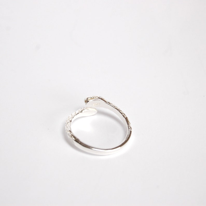 May include: Silver snake ring with a textured finish. The ring is open and adjustable.