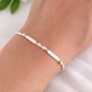 Puede incluir: Una taza de cerámica blanca con un asa negra y el texto "But First, Coffee" en un estilo manuscrito. La taza está sobre una superficie blanca. La taza mide aproximadamente 10 cm de alto.