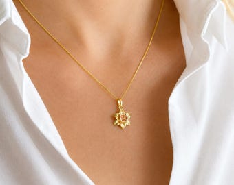 May include: A gold necklace featuring a delicate chain and a pendant shaped like a daffodil flower. The pendant has a polished gold finish with a central petal detail, suspended from a fine link chain that rests against a white collared shirt.