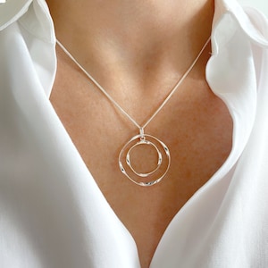 May include: A silver necklace featuring a double circle pendant. The circles are interlocked and have a textured finish.