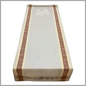 May include: A white table runner with brown and cream colored borders featuring a vine pattern. The runner is approximately 14 inches wide and 70 inches long.