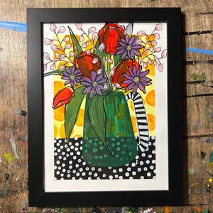 May include: Framed artwork featuring a vibrant floral arrangement. The painting showcases red tulips and purple flowers in a green vase with a black and white striped handle. The background has yellow and white accents.