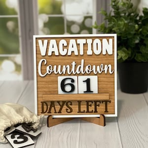 A wooden countdown sign with white text that reads 'Vacation Countdown 61 Days Left'. The sign is on a wooden stand and has a white background. The numbers 61 are displayed on the sign in black on white squares.