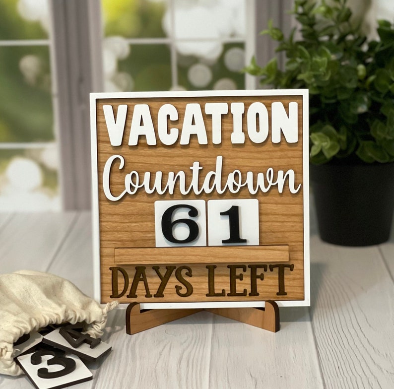 A wooden countdown sign with white text that reads 'Vacation Countdown 61 Days Left'. The sign is on a wooden stand and has a white background. The numbers 61 are displayed on the sign in black on white squares.