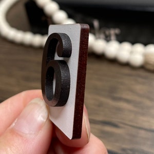 Close-up side view of a single white countdown number tile with a raised black number 6, showing the layered wood construction.