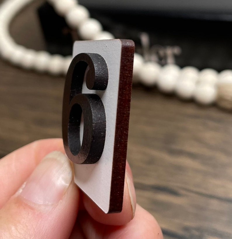 Close-up side view of a single white countdown number tile with a raised black number 6, showing the layered wood construction.