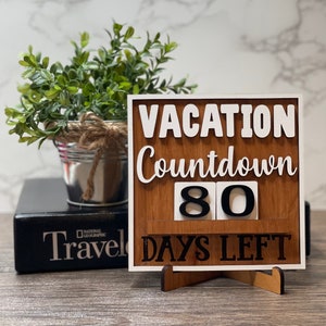 A wooden countdown sign with the text 'Vacation Countdown 80 Days Left' in white and black lettering. The sign is standing on a small wooden stand