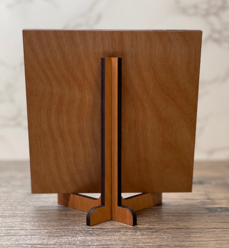 Wooden display stand shown from the back, featuring a natural wood grain panel supported by an interlocking wooden base on a rustic tabletop.