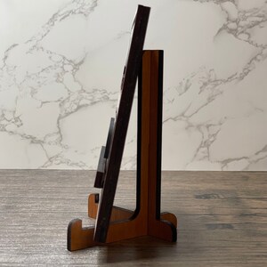 Side view of a wooden display stand holding a thin wooden sign, shown on a rustic tabletop with a marble-patterned background