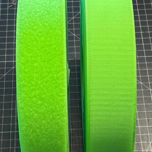 May include: Two rolls of bright green hook and loop fastener tape. The tape is rolled up and the edges are visible. The tape is made of a soft, fuzzy material.