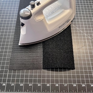 May include: A white iron with a black knob and a black hook and loop fastener tape on a black grid surface.