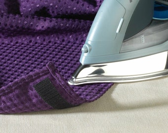 May include: A purple fabric with a black hook and loop fastener is being ironed with a gray iron. The iron has a silver soleplate and a black MAX button.