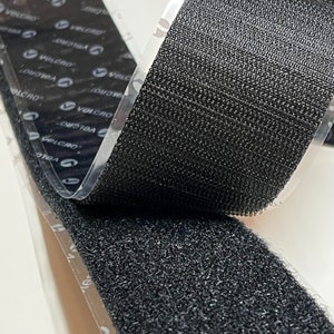 May include: Black hook and loop fastener tape with a clear adhesive backing. The tape is folded over to show the hook side and the loop side.