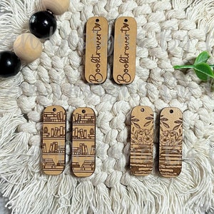 May include: Four laser cut wooden tags with different designs. Two tags feature the text "Booktrovert" and two tags feature a bookshelf design and a floral design.