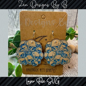 May include: A pair of dangle earrings featuring a cluster of skulls with a blue ink design on a light brown wooden base. The earrings are displayed on a rectangular brown card labeled Zen Designs By B and Handmade With Love.