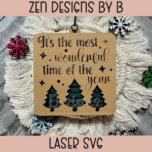 May include: A square wooden ornament featuring the engraved text It's the most wonderful time of the year, accented with four-pointed stars and three dark green pine trees at the bottom. The ornament has a black hanging loop at the top center.