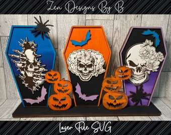 May include: Three wooden coffin-shaped displays labeled Zen Designs By B and Laser File SVG. The blue, orange, and purple coffins feature skull, floral, spider, bat, and pumpkin cutouts. The designs include intricate line art and layered wood elements.