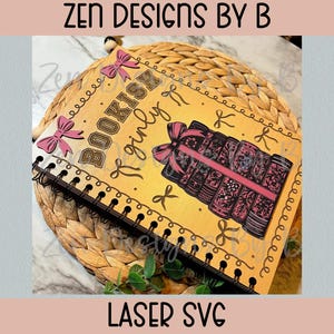 May include: A spiral-bound notebook with the words "Bookish & Girly" and a stack of books with a pink ribbon. The notebook has pink bows and decorative elements. The text "Laser SVG" is at the bottom.