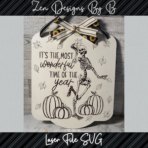 May include: A white rectangular wooden sign with rounded corners featuring a black line art illustration of a skeleton dancing among pumpkins and falling leaves. The text reads IT'S THE MOST wonderful TIME OF THE YEAR. A striped bow with sunflowers sits on top.