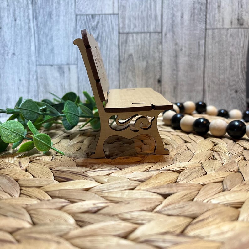 Puede incluir: Un peque&ntilde;o banco de madera con tallas intrincadas en el respaldo y las patas. El banco est&aacute; hecho de madera marr&oacute;n claro y est&aacute; sentado en una estera tejida.