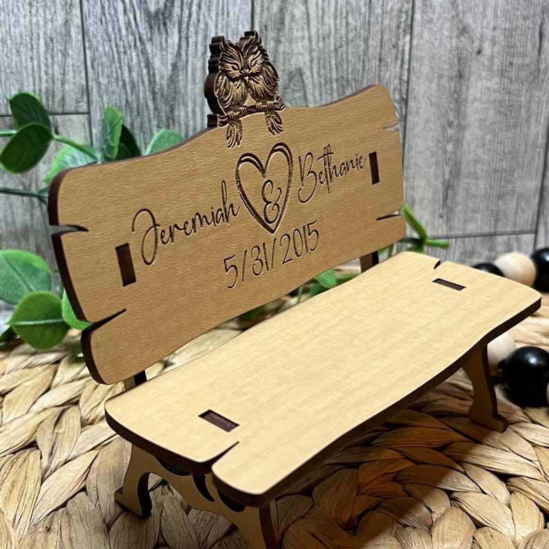 Puede incluir: Un banco de madera con un coraz&oacute;n y los nombres Jeremiah & Bethanie y la fecha 5/31/2015 grabados en &eacute;l. Dos b&uacute;hos est&aacute;n posados en la parte superior del banco.