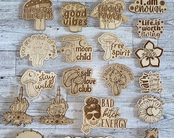 May include: A collection of twenty-four laser-cut wooden shapes featuring various mushroom, floral, and skull designs with engraved text including phrases like peace, hippie soul, groovy, good vibes, flower power, stay wild, and bad bitch energy.