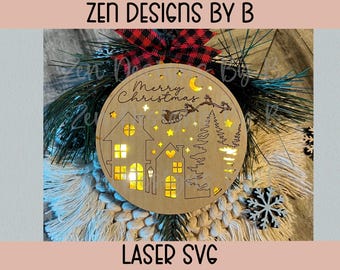 Può includere: Un addobbo natalizio circolare in legno con una scena tagliata al laser di case, pini, una luna crescente, stelle e una slitta con renne. Il testo Merry Christmas è inciso in alto. L'ornamento è illuminato da una calda luce gialla.