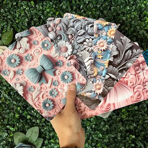 May include: A set of rectangular cards featuring embossed floral patterns and a prominent bow design. The cards display various color palettes including soft pink, light blue, grey, and yellow, with intricate sculpted petals and leaves.