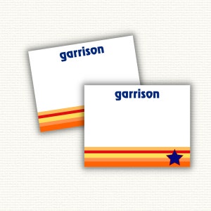May include: Two white note cards with the name "garrison" printed in blue letters. The cards have a red, yellow, and orange striped design with a blue star on the bottom card.
