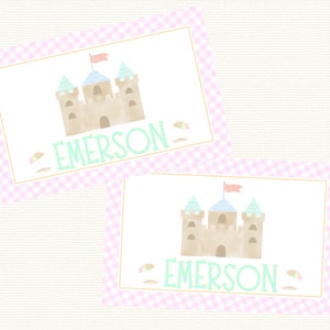 May include: Two pink and white gingham place cards with a sandcastle illustration and the name "EMERSON" in green text.