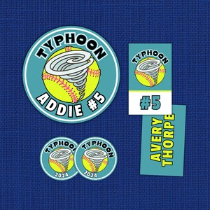 May include: A collection of softball-themed stickers and labels. The designs feature a yellow softball with a gray tornado graphic, the word "TYPHOON", and player names and numbers. The background is a textured blue.