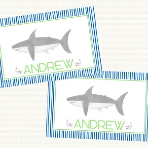 May include: Two blue and white striped place cards with a gray shark illustration and the name "ANDREW" in green text.
