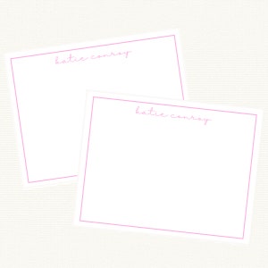 May include: Two blank white note cards with pink borders and the name "katie conroy" written in pink cursive on each card.