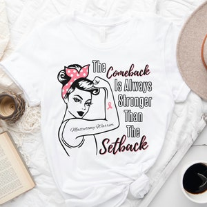 Könnte beinhalten: Weißes T-Shirt mit einer schwarzen und pinkfarbenen Grafik einer Frau mit einem rosa Band und dem Text "The Comeback Is Always Stronger Than The Setback". Der Text "Mastectomy Warrior" ist ebenfalls in der Grafik enthalten.