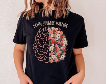 May include: Black t-shirt with a pink outline of a brain with flowers inside. The text "Brain Surgery Warrior" is printed on the shirt.