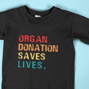 May include: Black t-shirt with the text "ORGAN DONATION SAVES LIVES." in a vintage style with rainbow colors.