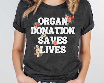 May include: A dark gray t-shirt with a white graphic that reads "Organ Donation Saves Lives" with floral accents.
