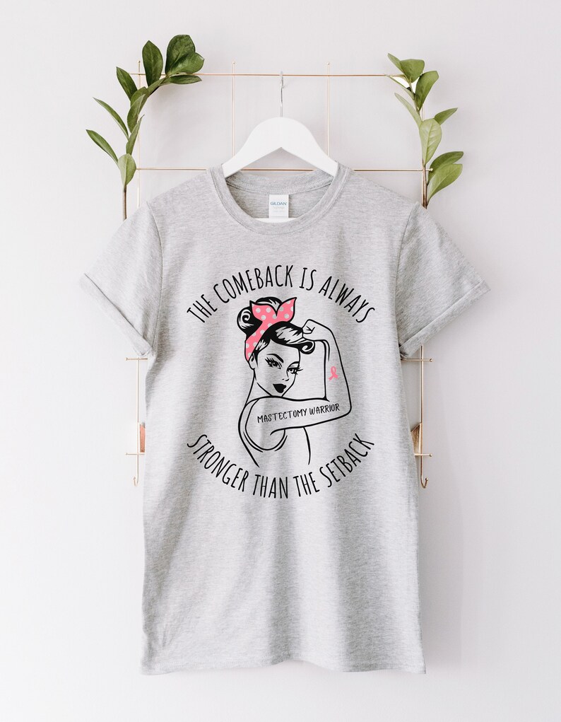 May include: Gray t-shirt with a black graphic of a woman with a pink ribbon on her arm. The text on the shirt reads "The comeback is always stronger than the setback" and "Mastectomy Warrior".
