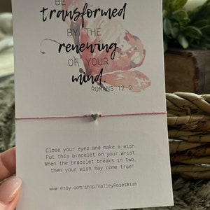 May include: A pink and white watercolor butterfly with the text "BE transformed BY THE renewing OF YOUR mind. ROMANS 12:2" on a white card. The card also includes instructions for a wish bracelet: "Close your eyes and make a wish. Put this bracelet on your wrist. When the bracelet breaks in two, then your wish may come true!" and a website address: "www.etsy.com/shop/ValleyRosesWish".