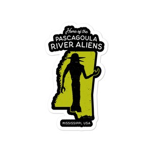 May include: A sticker featuring a black silhouette of an alien with a large head and wide eyes, standing in front of a yellow outline of the state of Mississippi. The text "Home of the Pascagoula River Aliens" is above the alien, and "Mississippi, USA" is below.